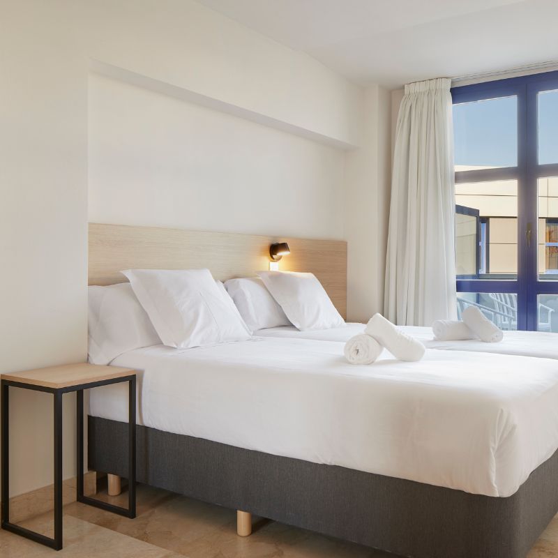 Imagen mostrando una
            habitación del hotel con una cama blanca y vistas al patio.